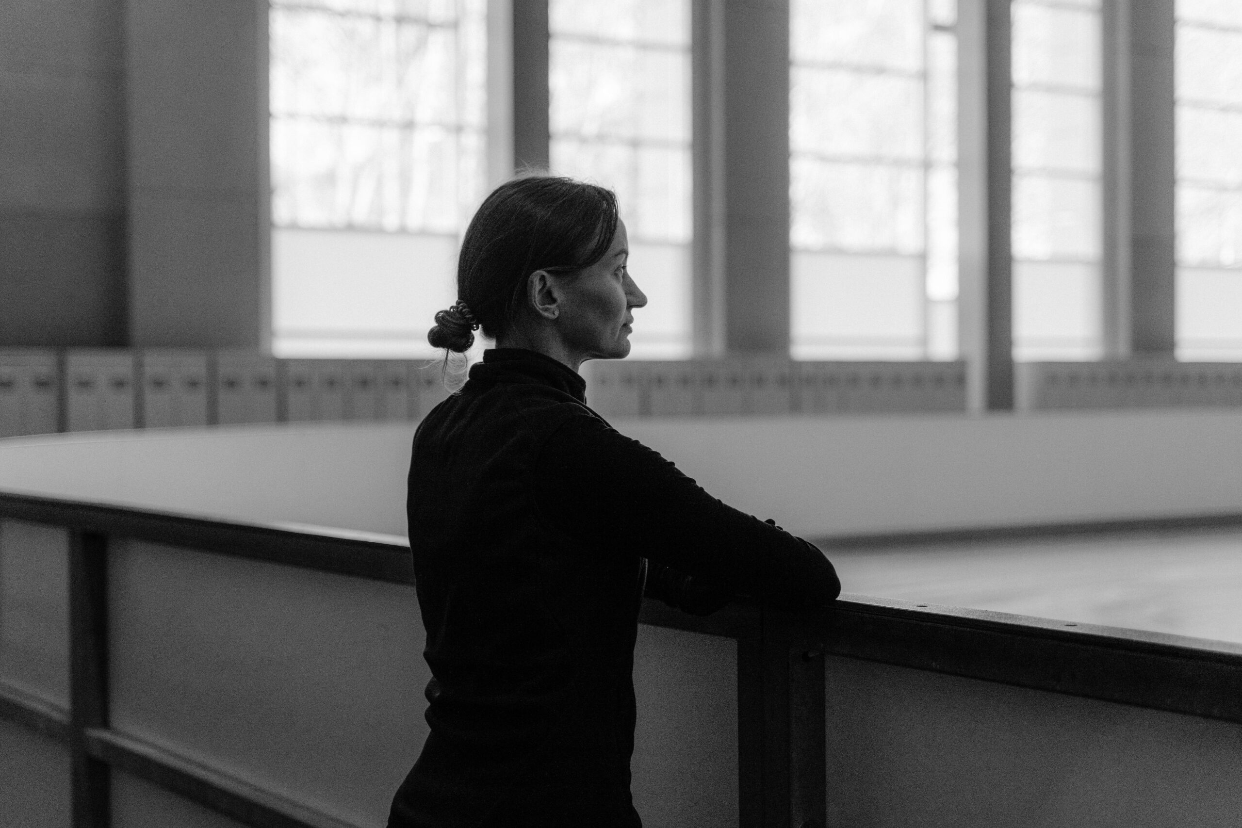 A woman in a black and white indoor setting, looking thoughtfully into the distance.